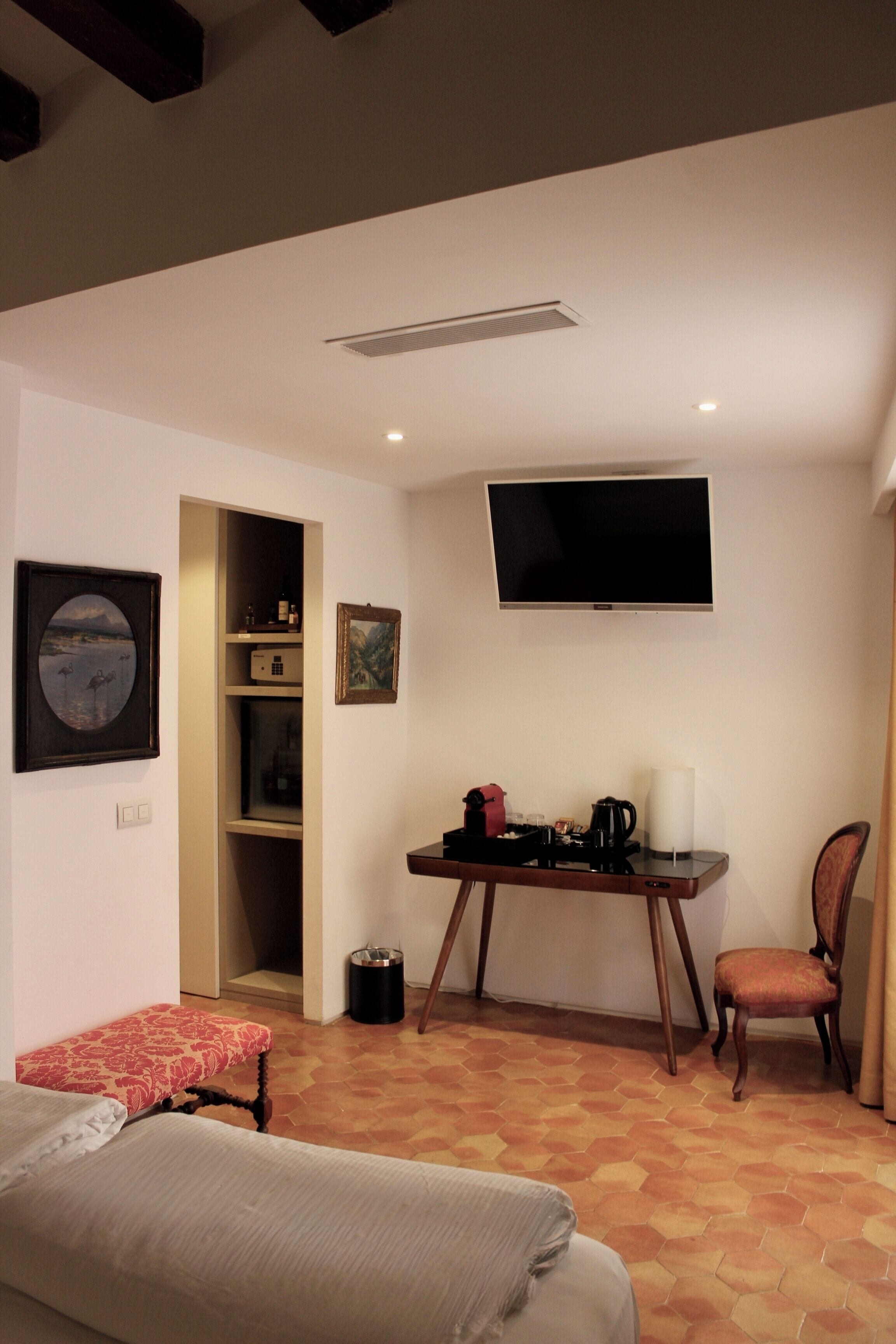 A hotel room with a bed, a desk with a chair, a TV, and a small seating area.