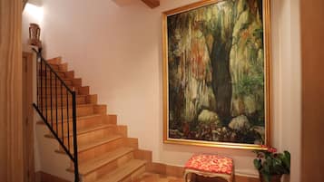 Una escalera de madera con barandillas negras que lleva a un rellano con un banco y un cuadro grande enmarcados con una escena de bosque.