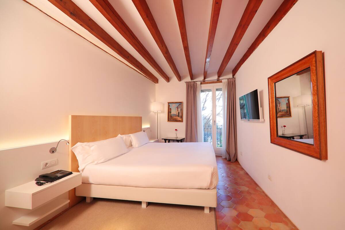 A hotel room with a large bed, bedside table, lamp, and a mirror on the wall.