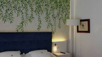 A neatly made bed with white linens, a blue headboard, and a wall with a green leafy pattern.