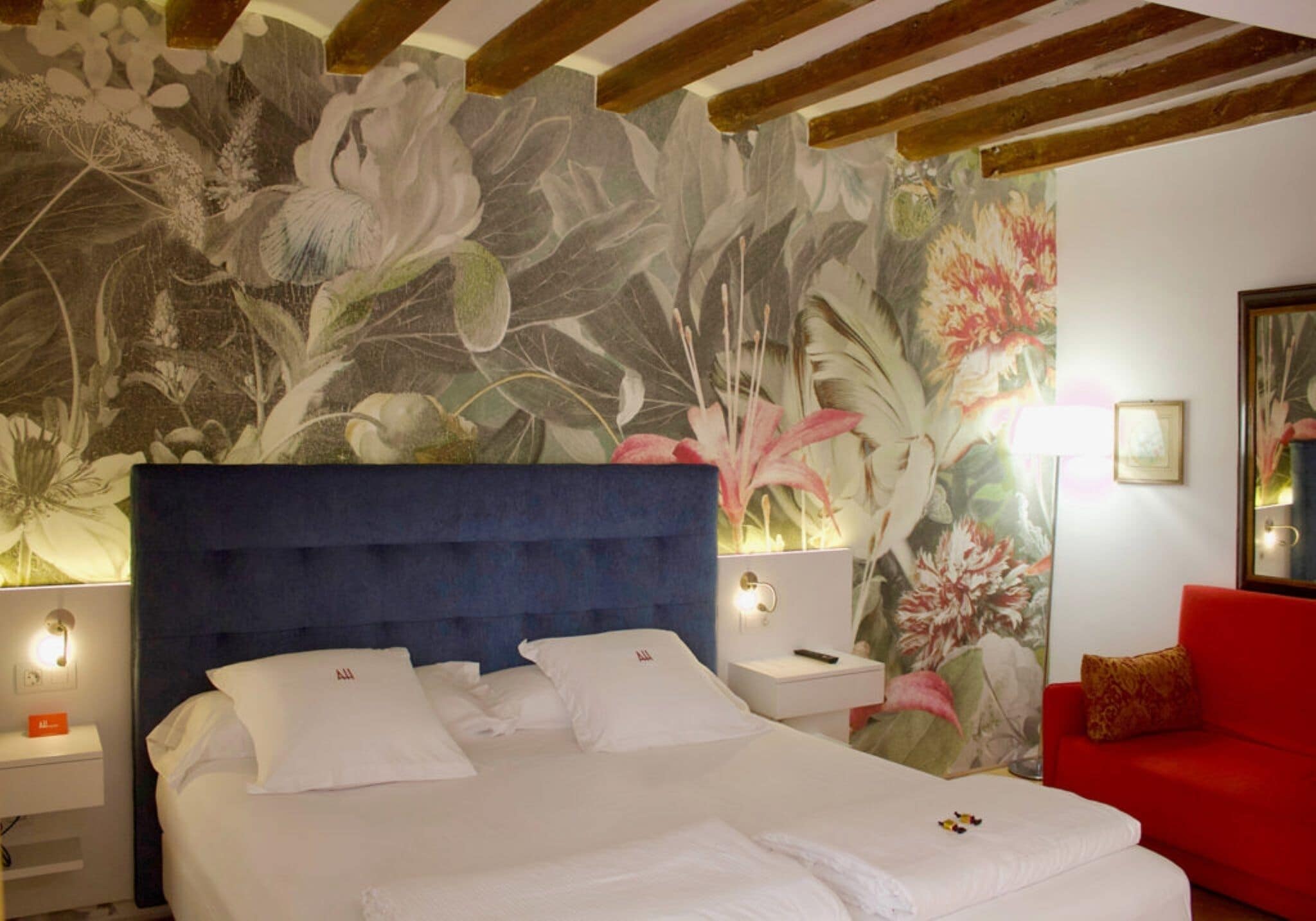 Habitación de hotel con una cama grande, un sofá rojo y un mural floral en la pared.