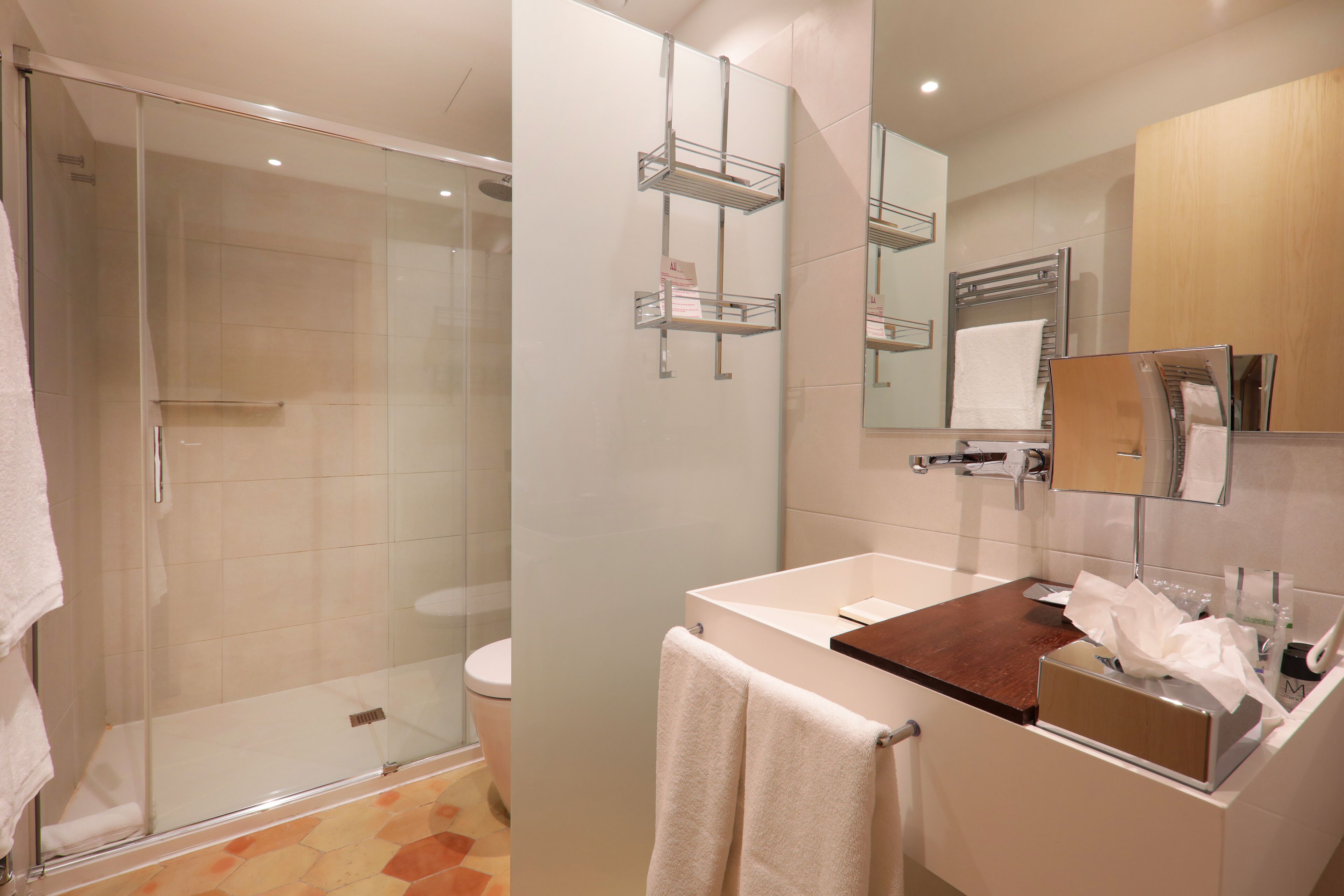 Un baño moderno con cabina de ducha de vidrio, inodoro, lavamanos con encimera de madera y espejo con una toalla colgada en la pared.