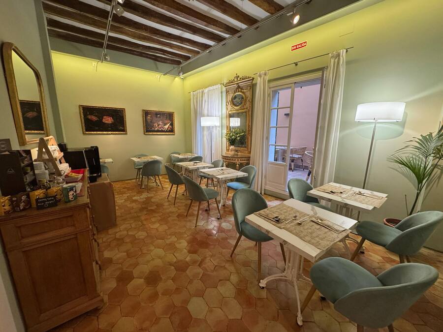 Un comedor con piso de diseño hexagonal, mesas con sillas, un espejo, obras de arte enmarcadas y un letrero que indica que no hay salida.