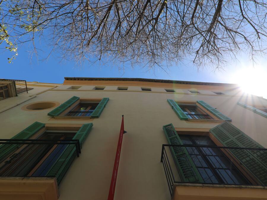 Un edificio con múltiples ventanas y balcones, que destaca un poste rojo en el centro y un cielo azul despejado.