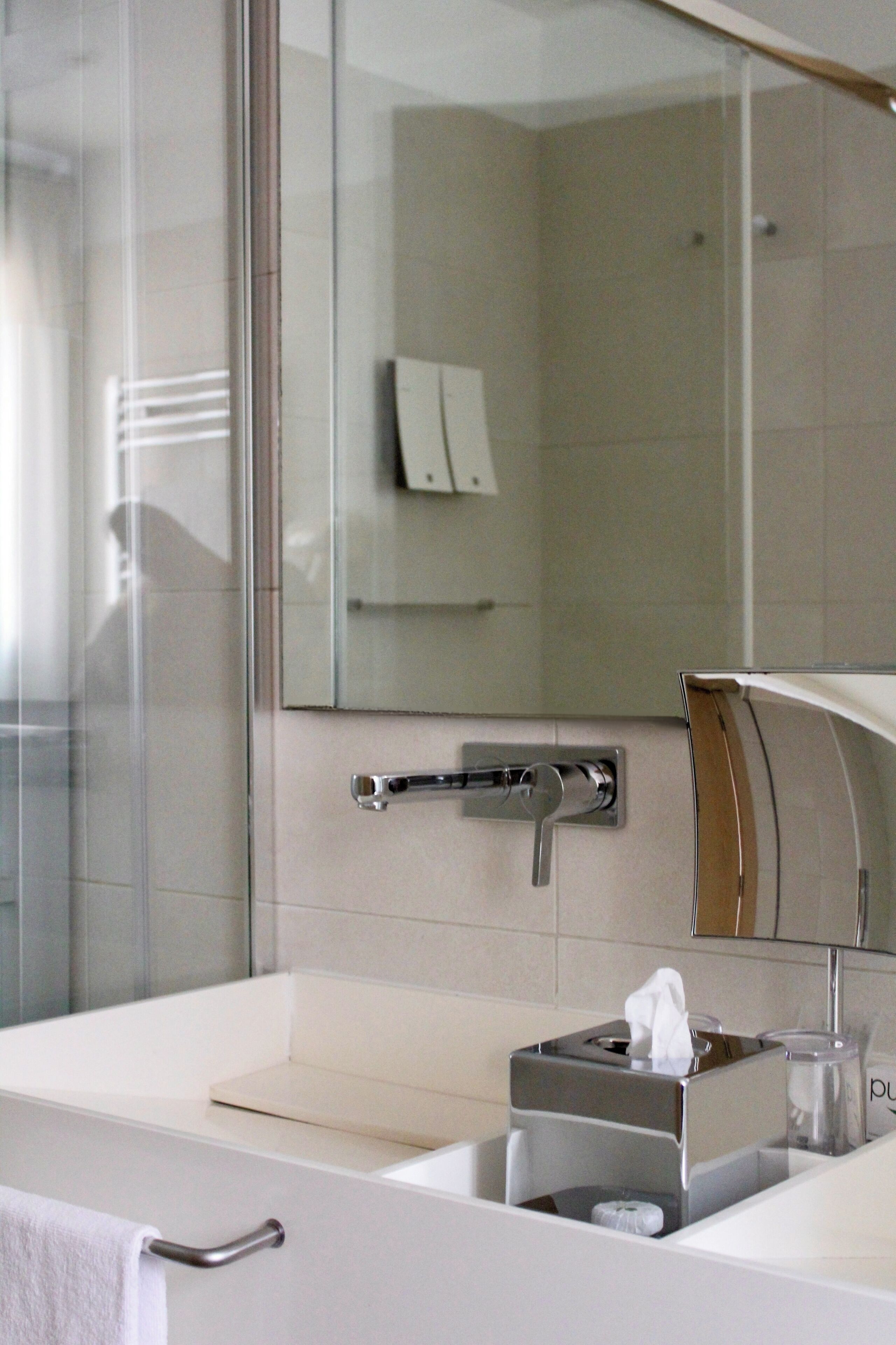 Un baño moderno con cabina de ducha de vidrio, un lavamanos blanco con toallero y un espejo sobre el lavamanos.