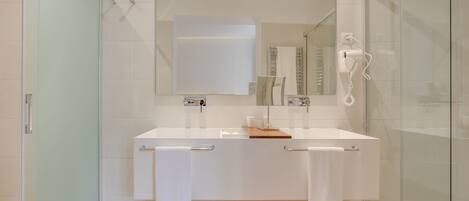 Un bagno moderno con box doccia in vetro, un lavandino bianco con un vassoio in legno e uno specchio grande sopra il lavandino.