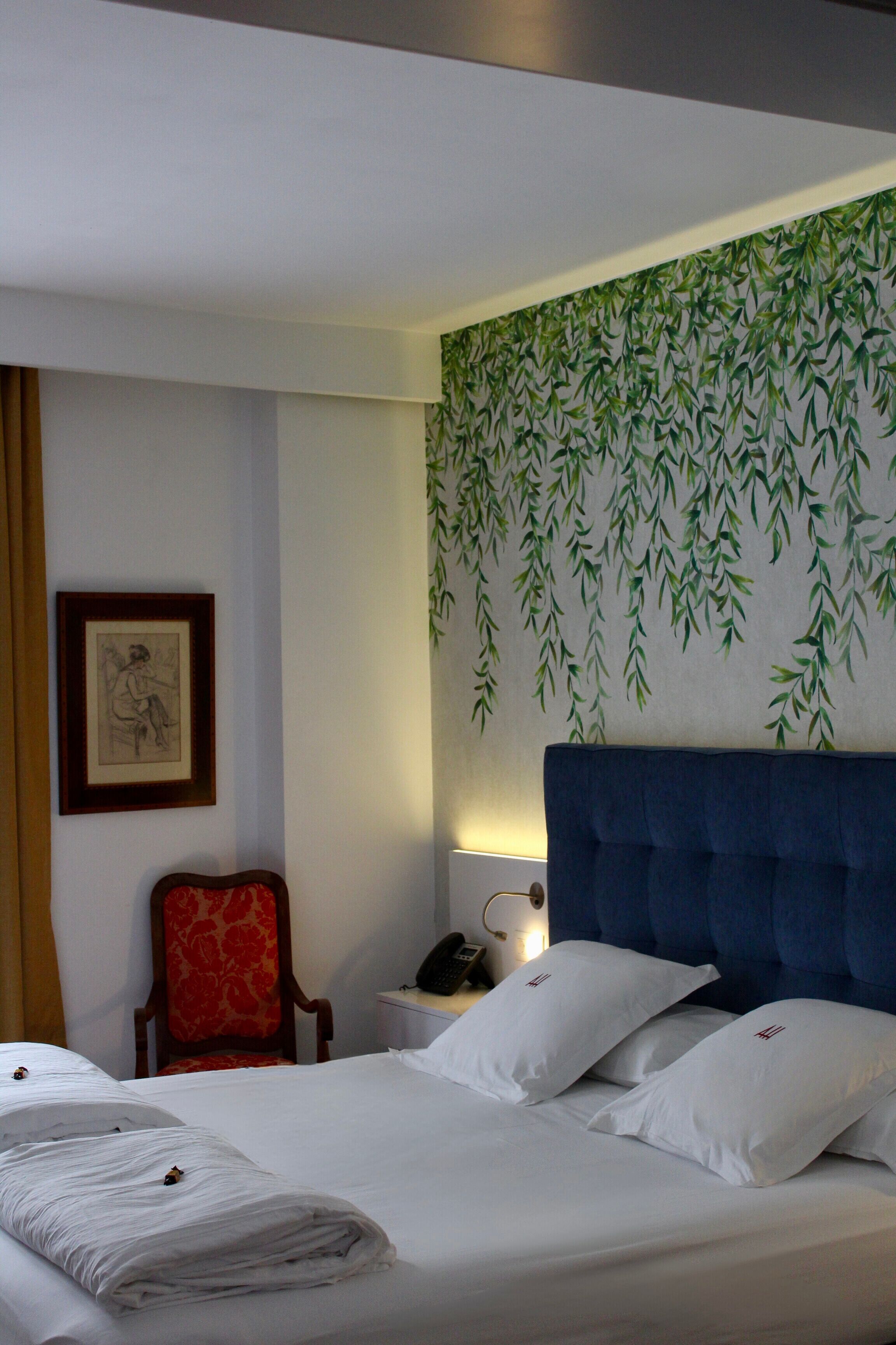 A hotel room with a bed, a chair, a nightstand, and a wall with a bamboo leaf pattern.