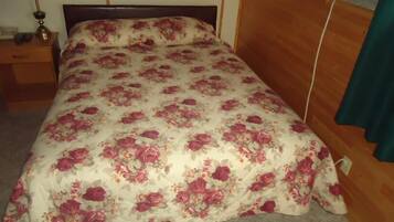 A bed with a floral bedspread, a wooden headboard, a nightstand with a lamp, and a wooden floor.