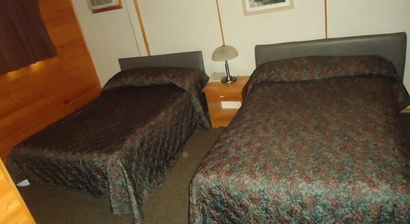Una habitación con dos camas individuales, paredes de madera, una mesita de noche con lámpara y una pequeña mesa.