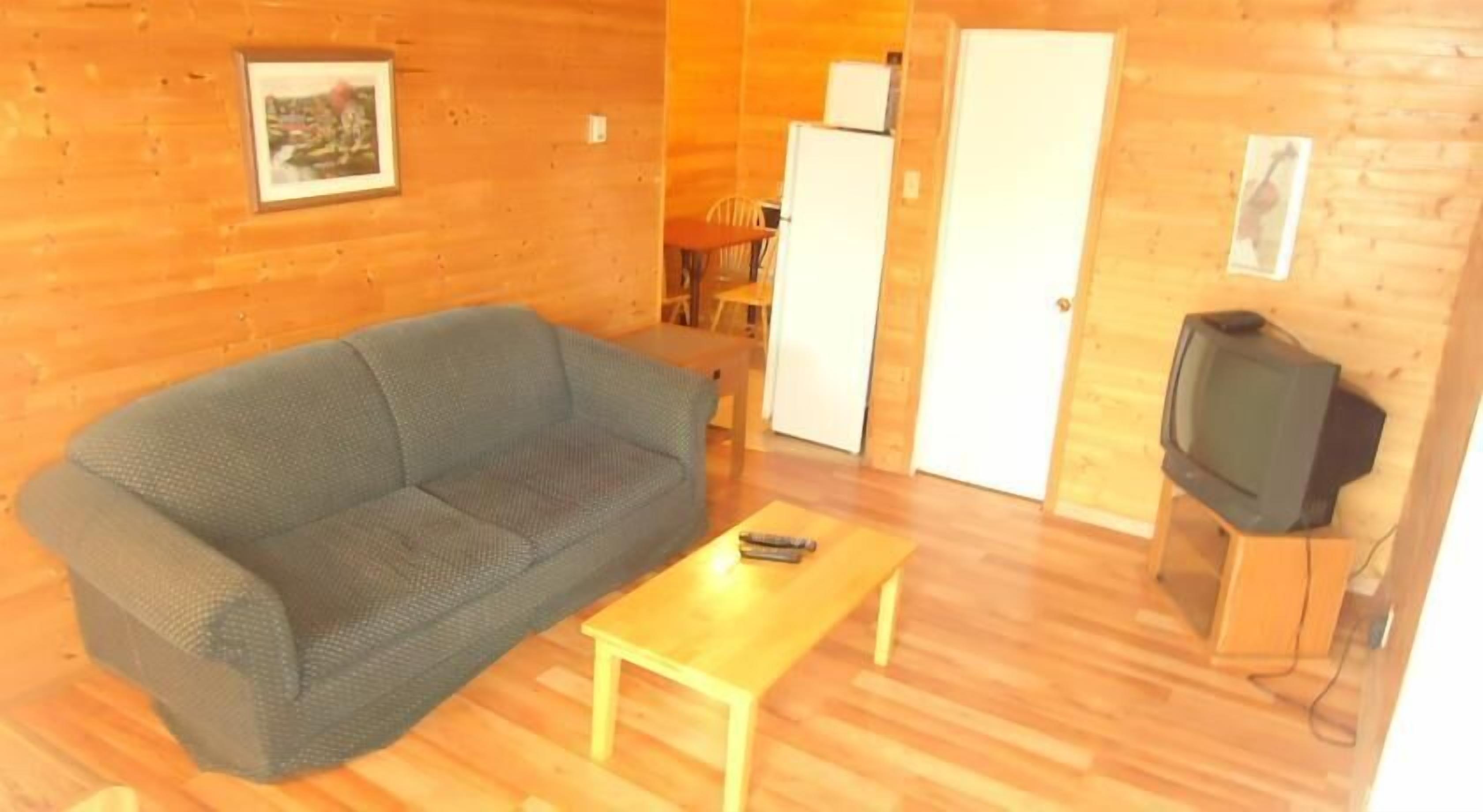 A cozy room with a grey sofa, a wooden coffee table, a television on a wooden stand, and a door leading to another room.