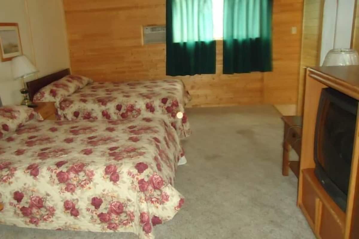 A hotel room with two beds, a wooden headboard, a television, and a window with green curtains.