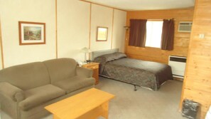 Una habitación pequeña y acogedora con una cama individual, un sofá, una mesita de noche y una mesa de madera.