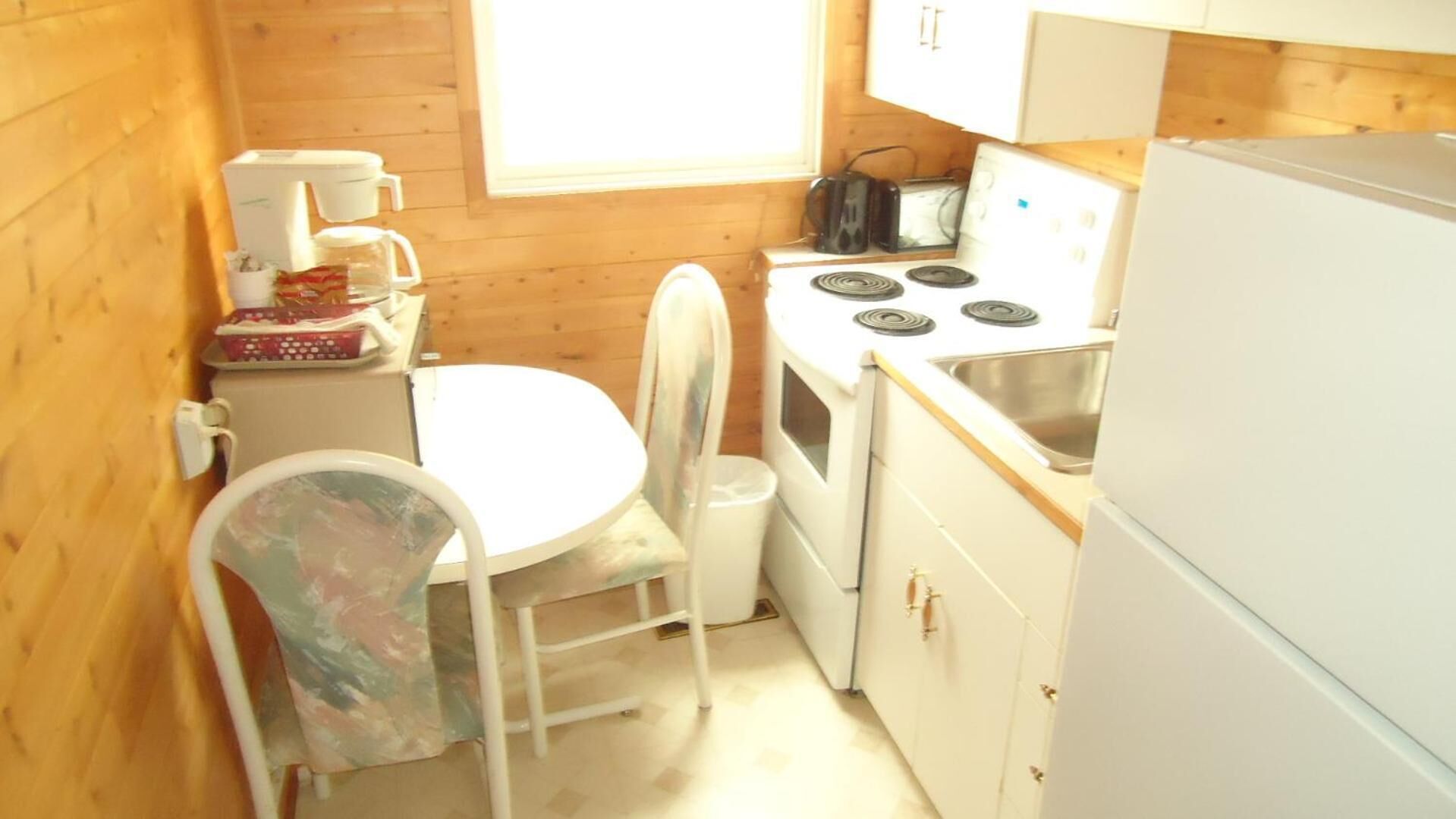 Una cocina compacta con estufa, pileta y una pequeña mesa de comedor con una silla.