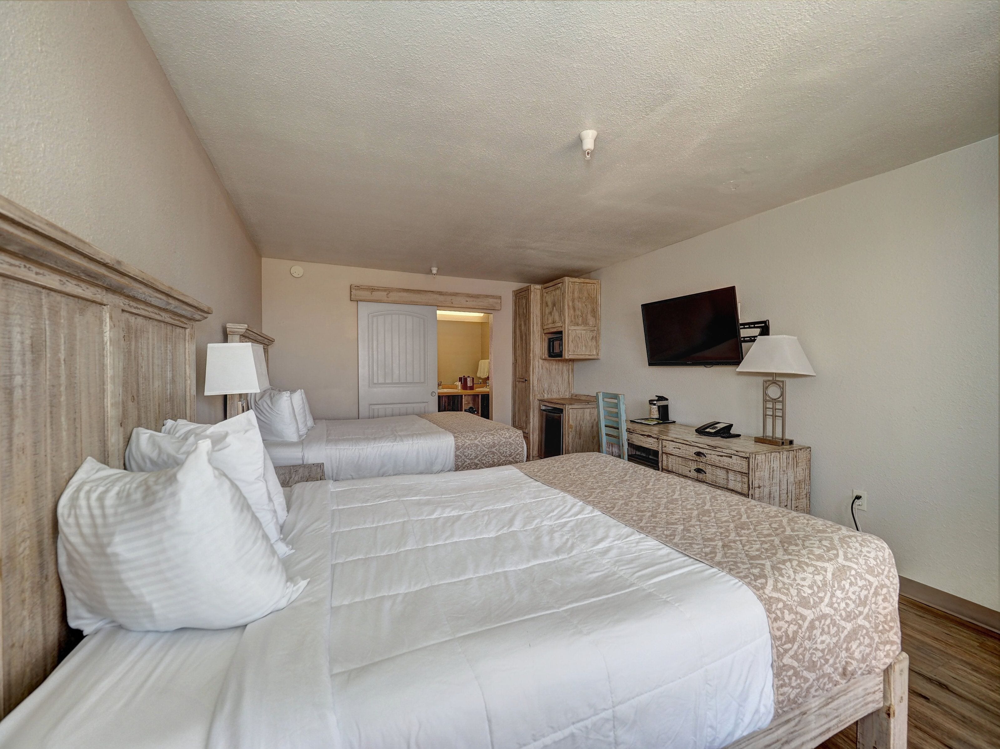 A hotel room with two beds, a television, a desk with a lamp, and a wardrobe.