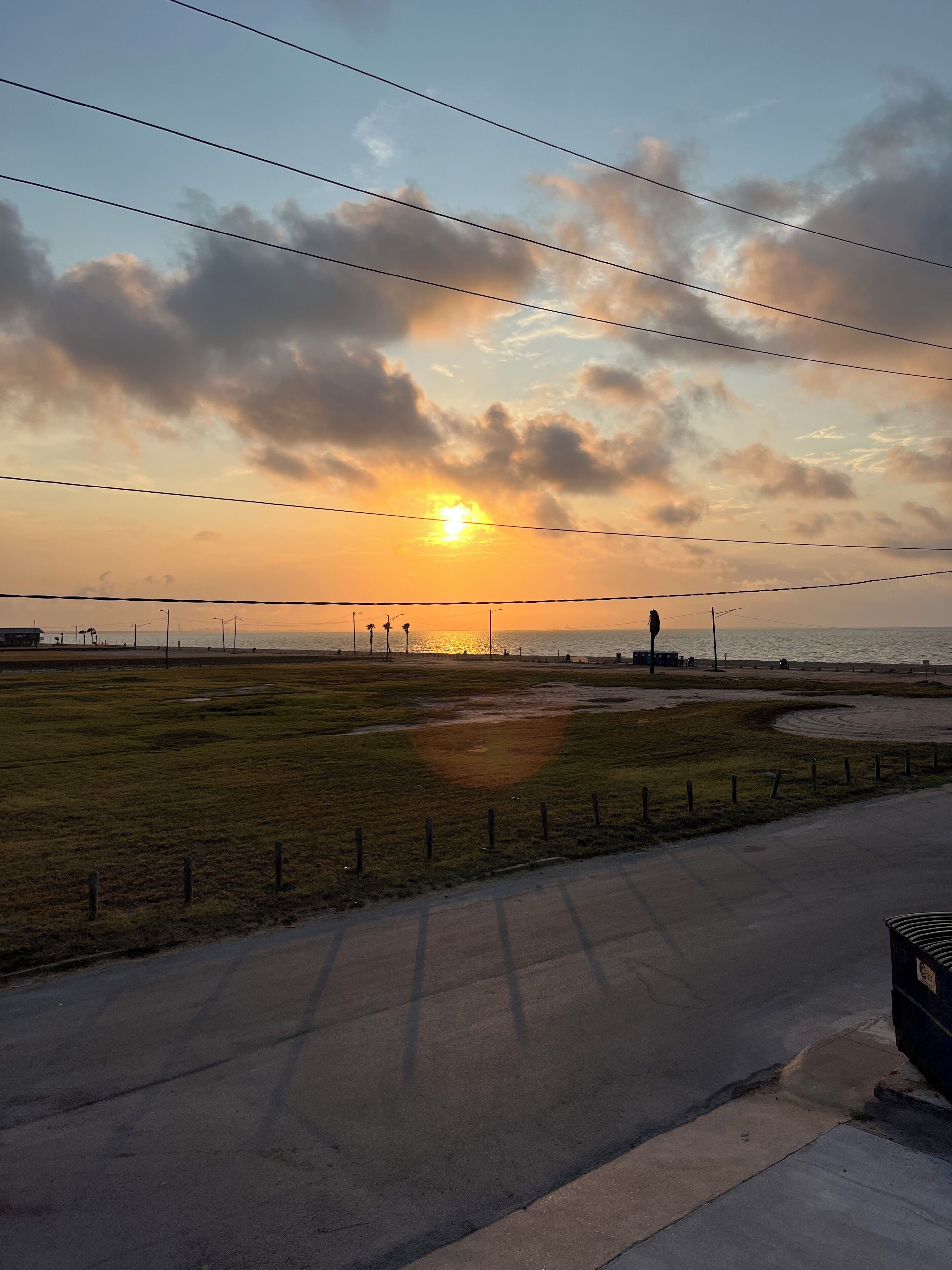 A sunset over a coastal area with a road and grassy fields.