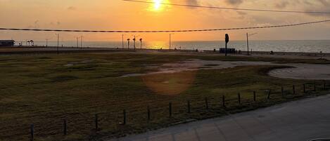 A sunset over a coastal area with a road and grassy fields.