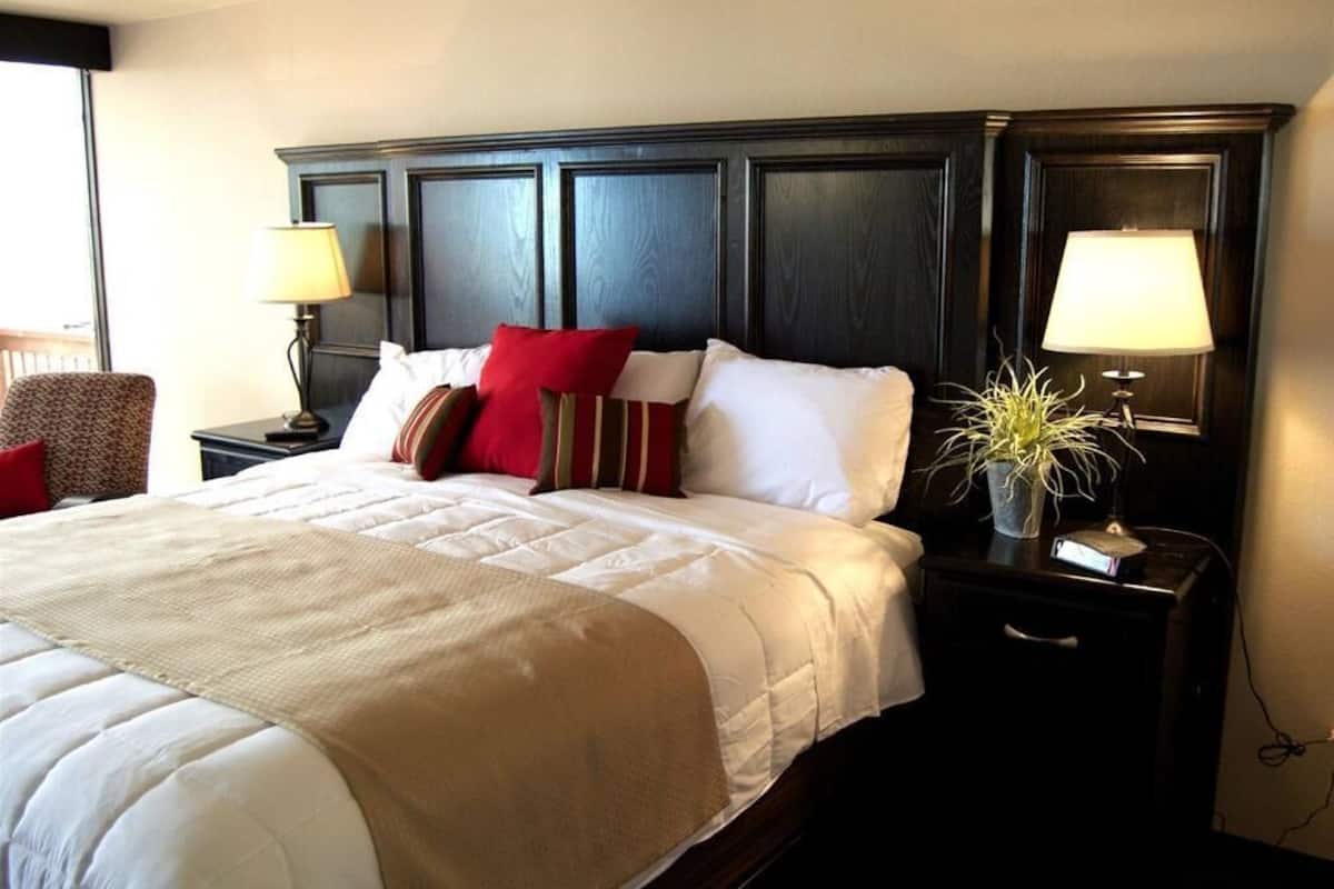 A hotel room with a large bed, two bedside tables with lamps, a chair, and a potted plant.