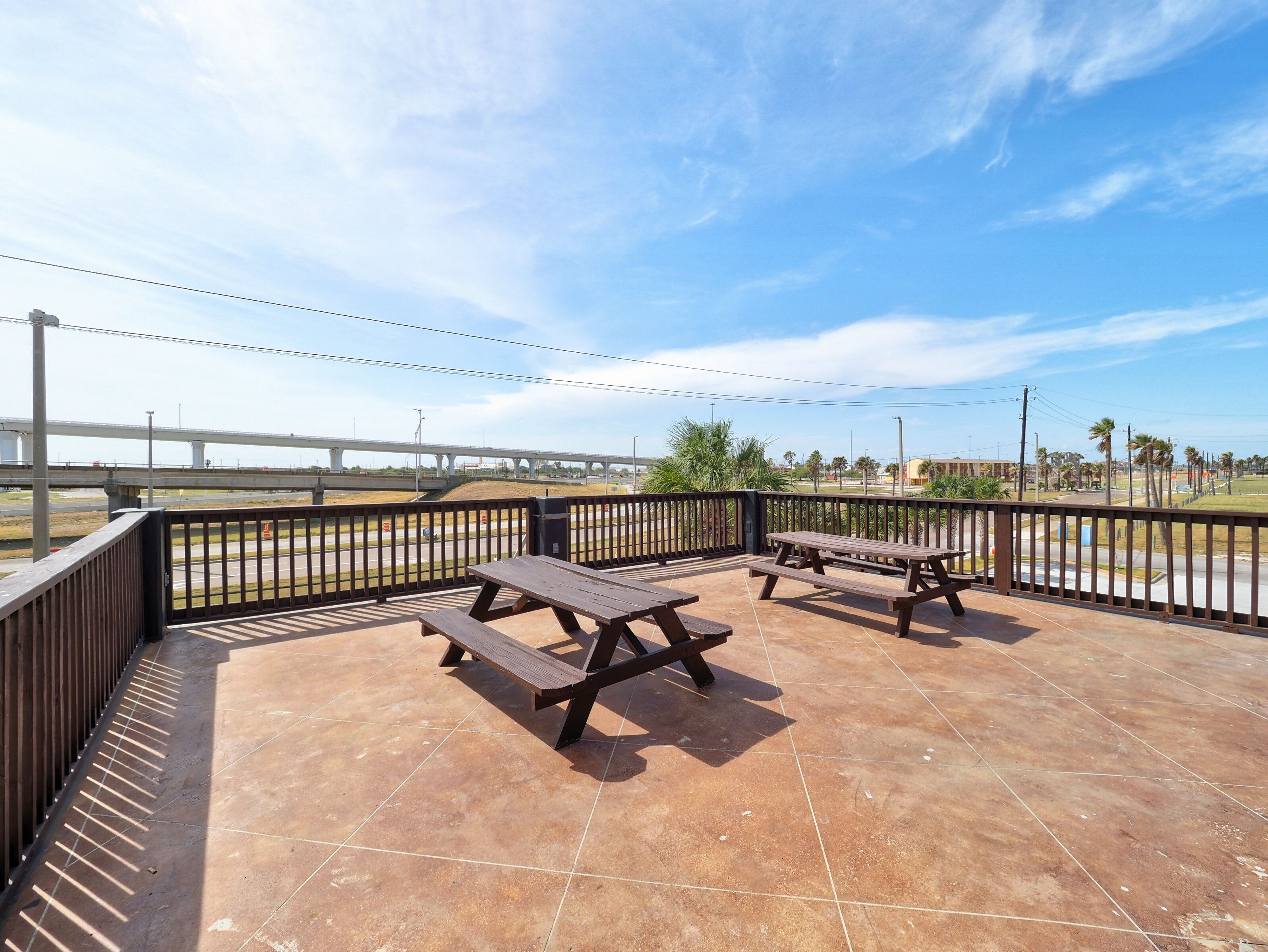 A patio area with picnic tables and a view of a bridge and palm trees.