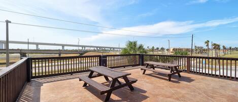 A patio area with picnic tables and a view of a bridge and palm trees.