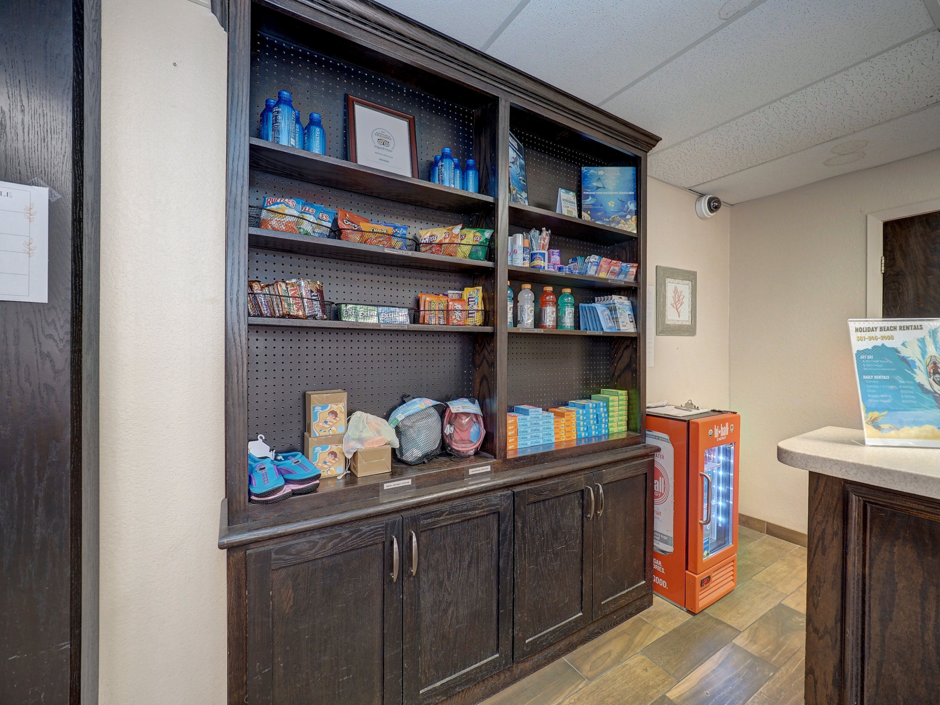 A reception area with a wooden counter, shelves stocked with snacks and beverages, and a holiday beach rentals poster.