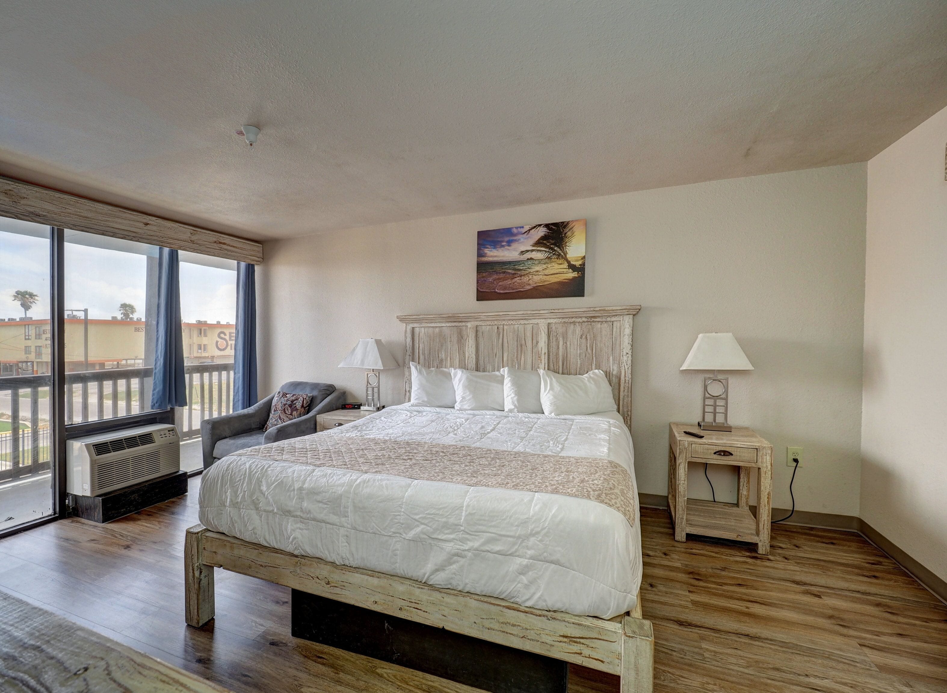 Een slaapkamer met een groot bed, een stoel, een nachtkastje, een lamp en een schilderij aan de muur.