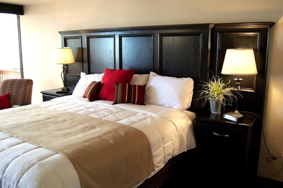 A hotel room with a large bed, two bedside tables with lamps, a chair, and a potted plant.