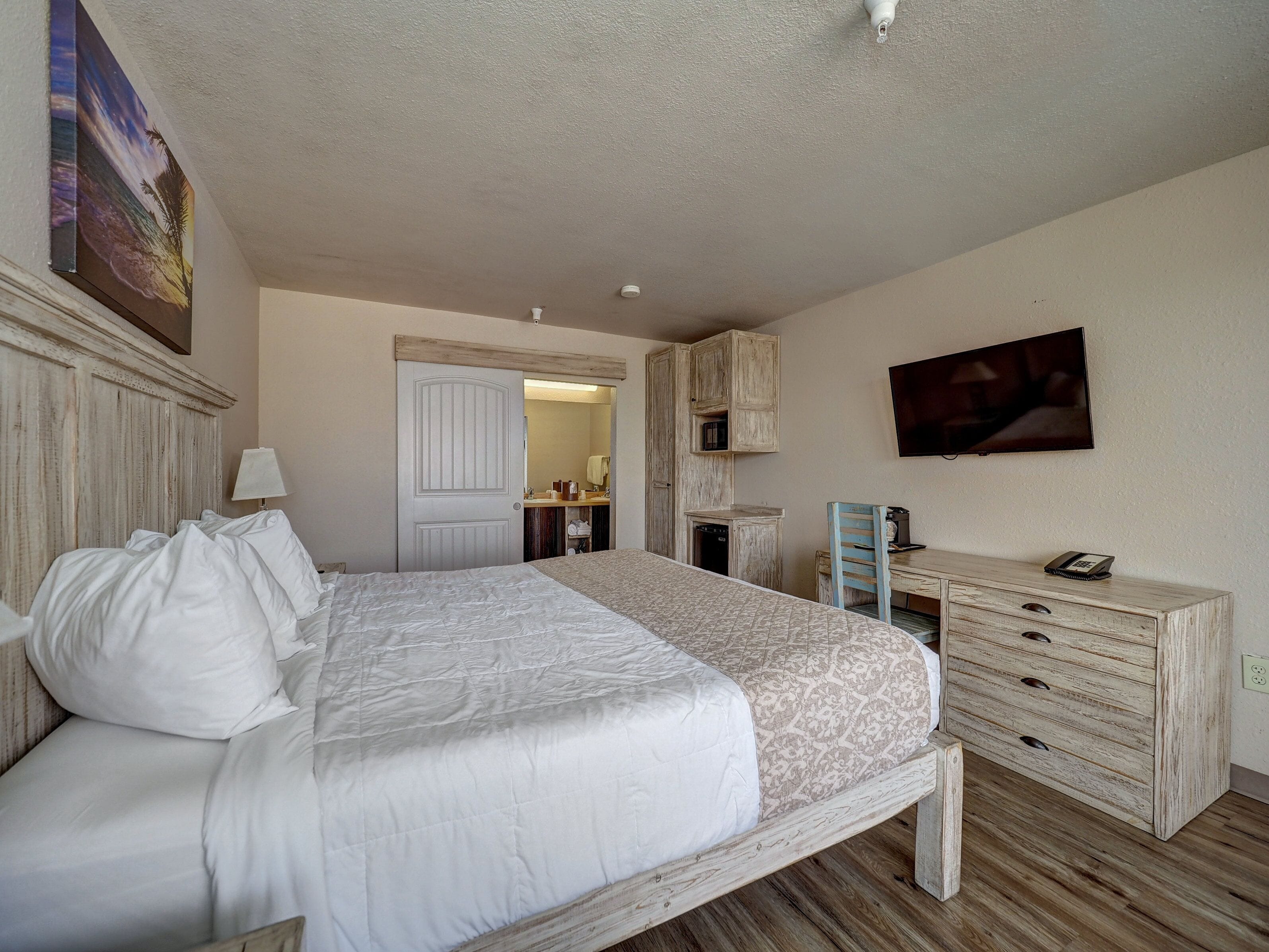 A bedroom with a bed, a dresser, a television, and a door leading to a bathroom.