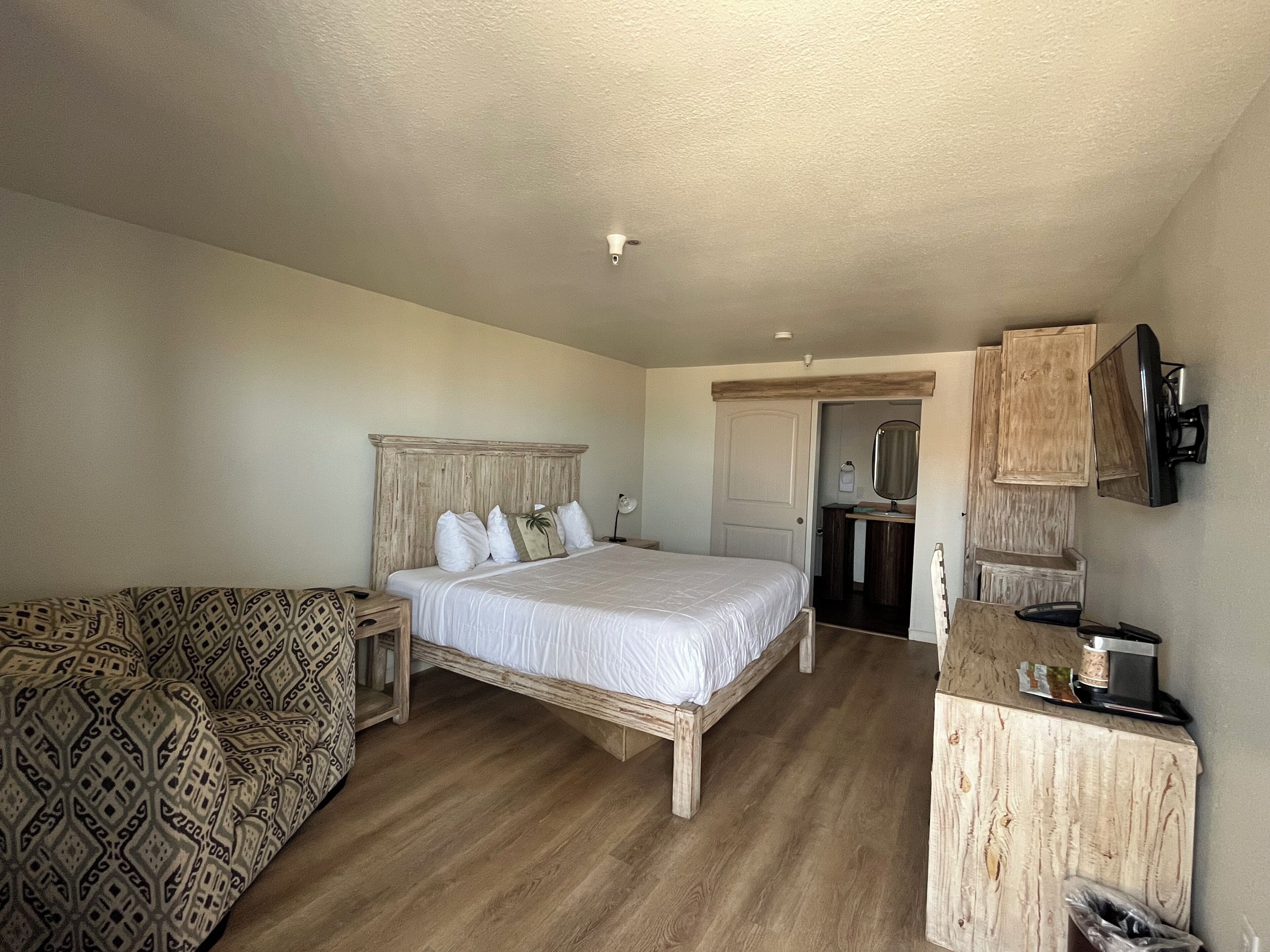 Un dormitorio con una cama de madera, un sofá estampado, un aparador de madera y un televisor montado en la pared.