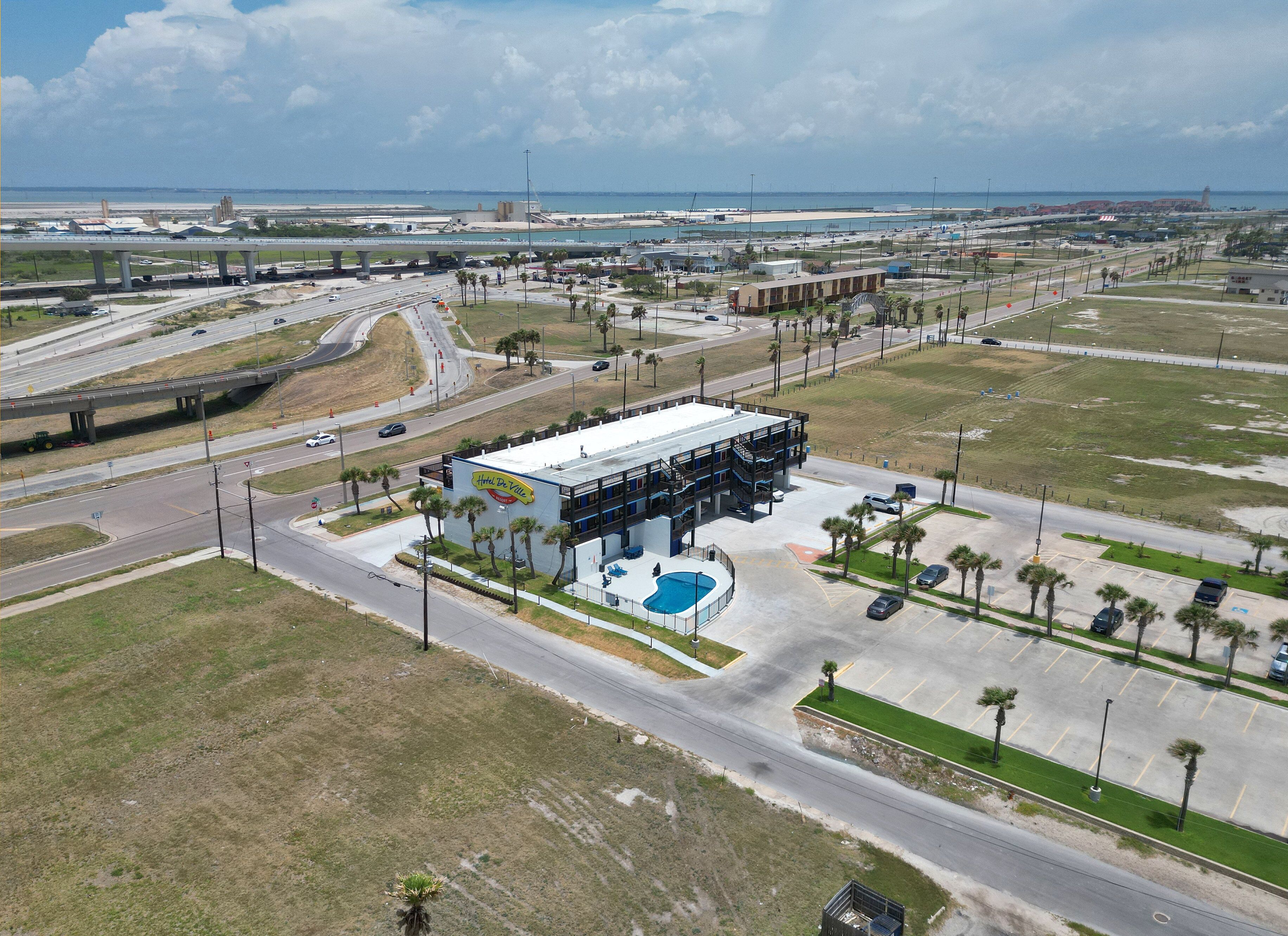 An aerial view of a hotel with a swimming pool, located near a highway and beach.