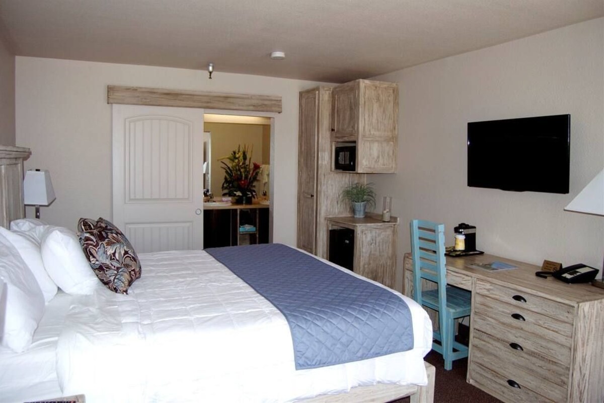Un dormitorio con cama, escritorio, silla, televisor y puerta que da a otra habitación.