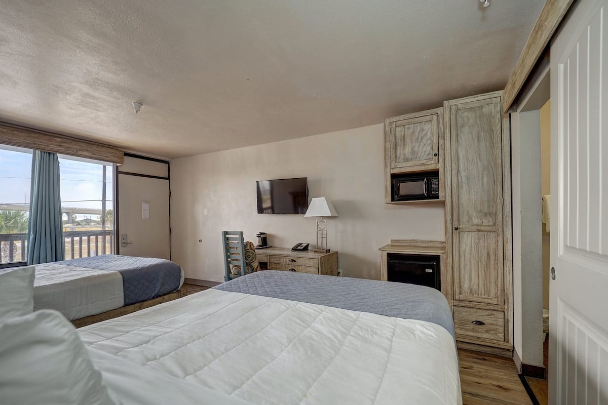 A bedroom with two beds, a TV, a microwave, a desk, and a wardrobe.