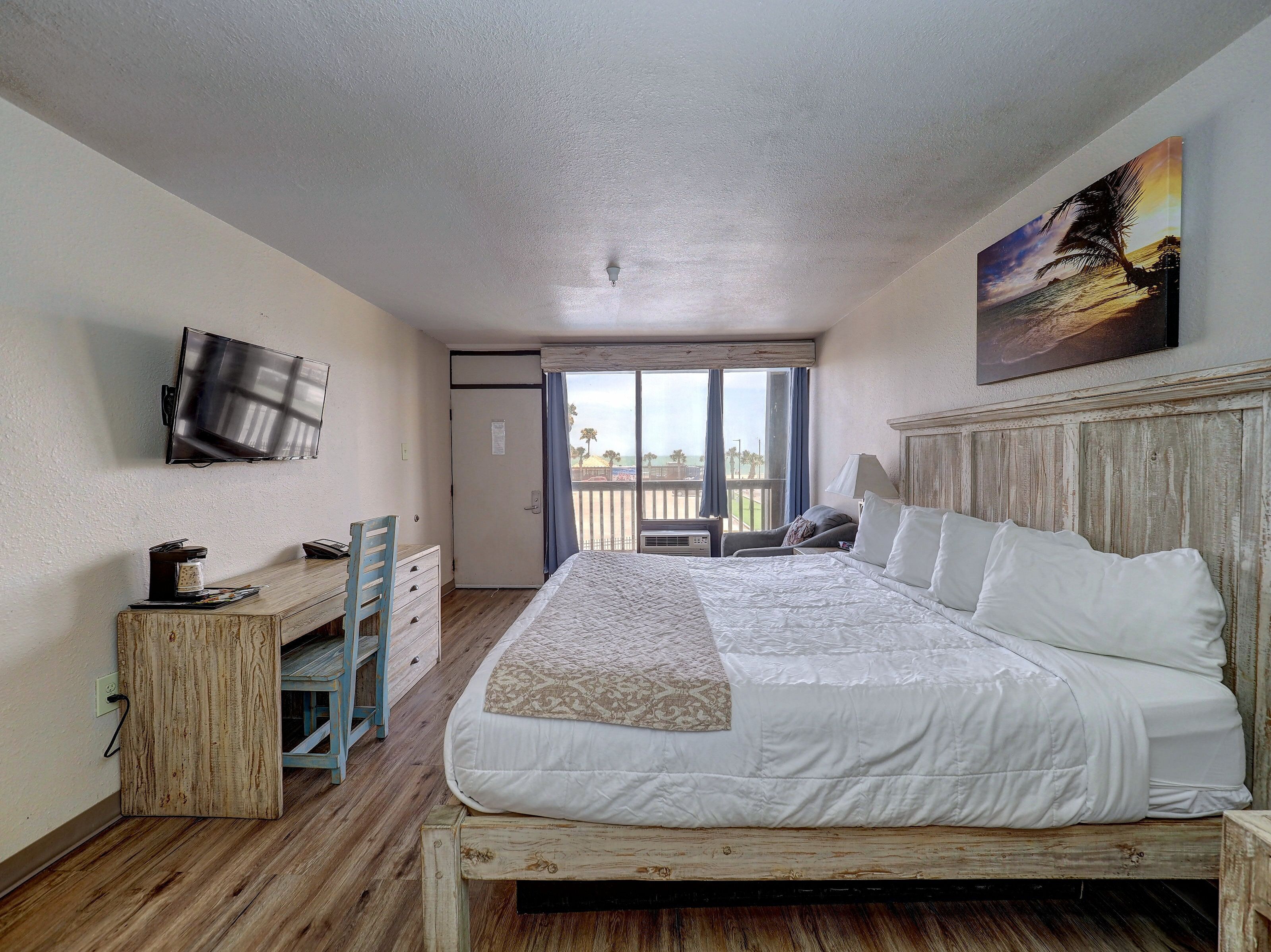 A bedroom with a bed, a desk with a chair, a television, and a balcony with a view.