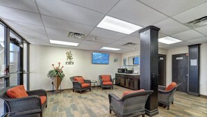 A lobby with wicker chairs, a reception desk, a coffee station, and a large screen. - Hotel De Ville (Corpus Christi)