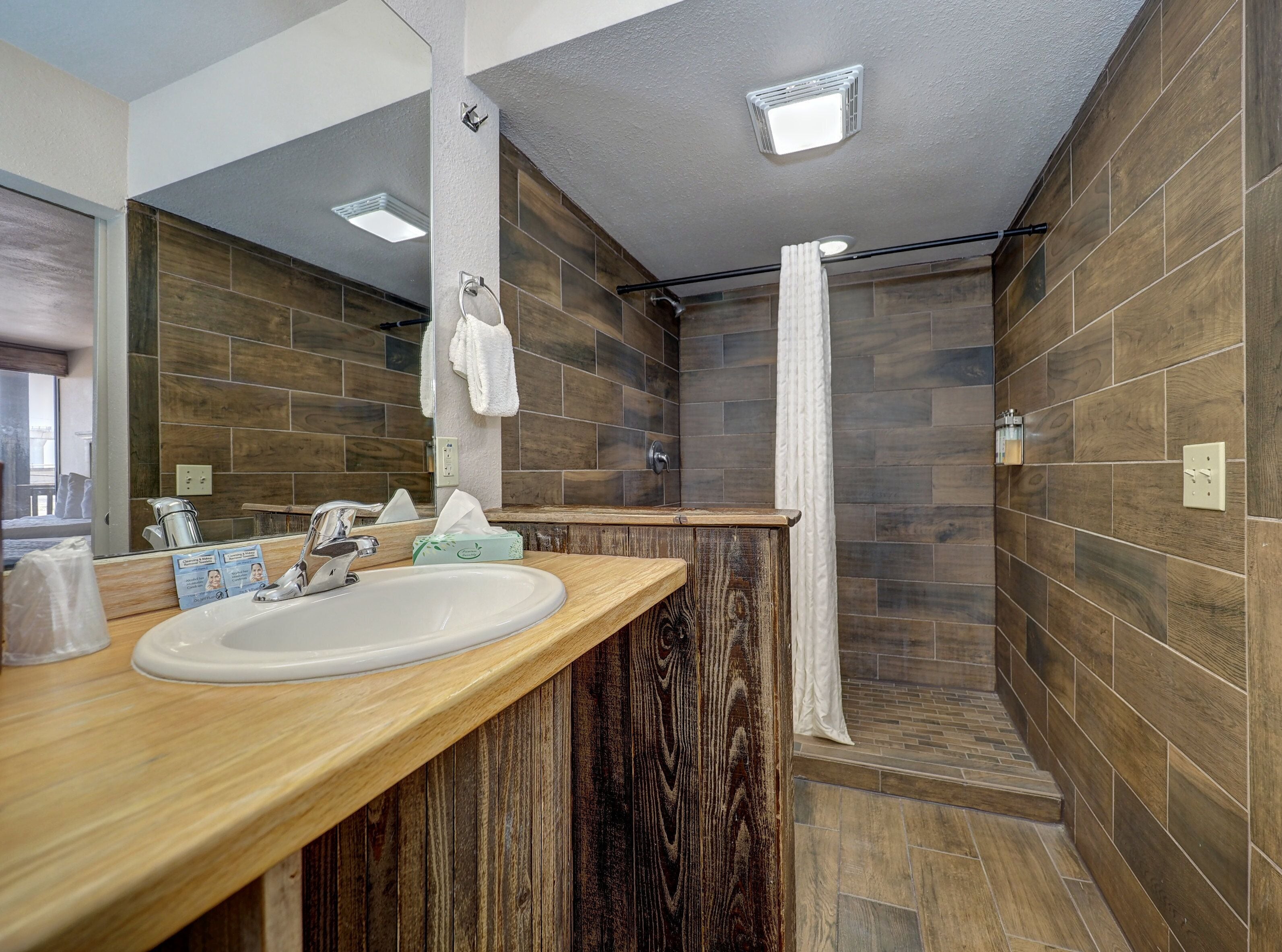 A modern bathroom with a wooden vanity, a large mirror, and a shower area.