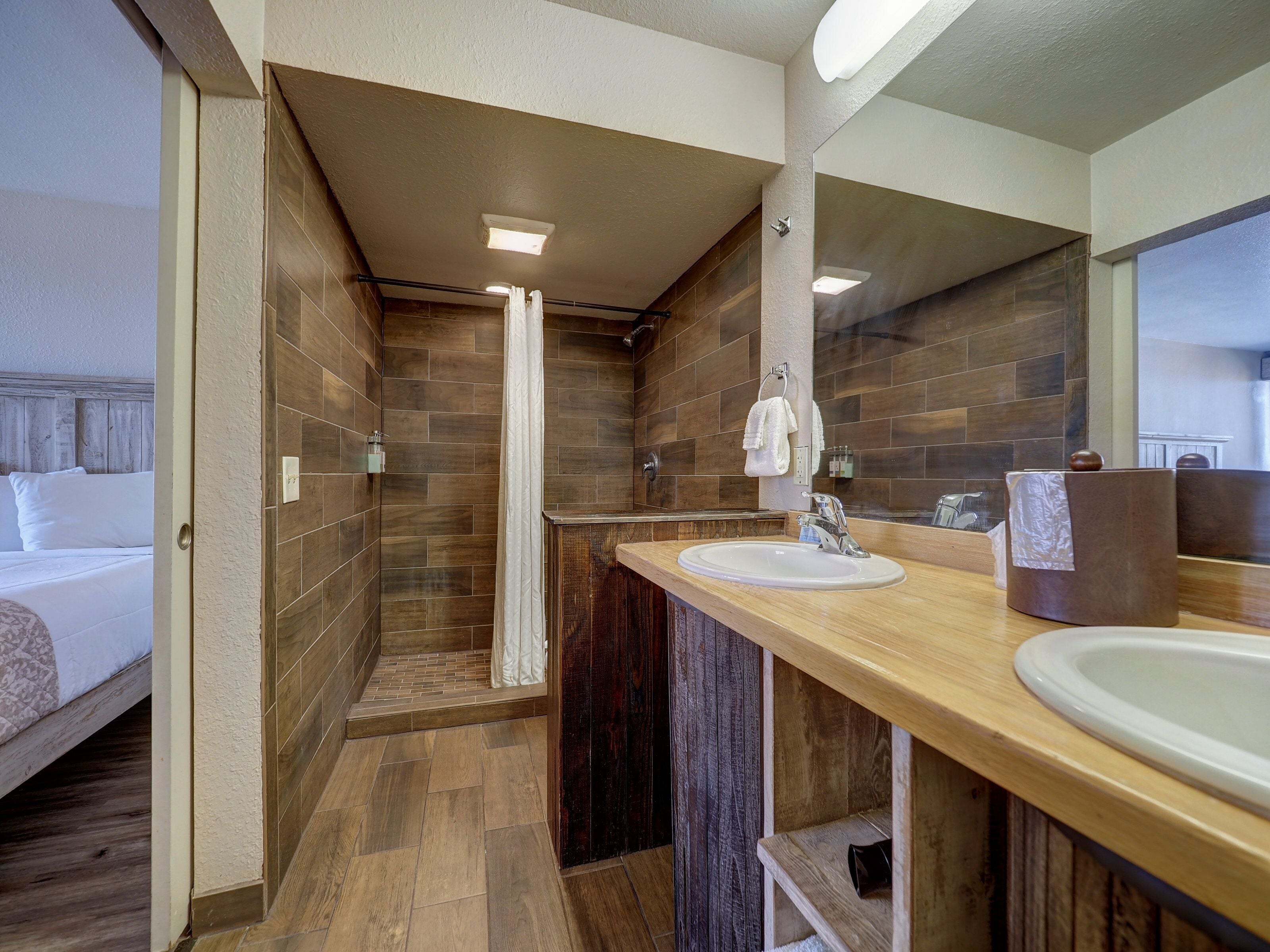 A modern bathroom with a wooden vanity, a large mirror, and a shower area.