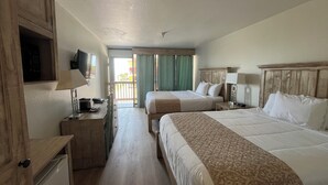 A hotel room with two beds, a desk with a lamp, a television, and a balcony with a view. - Hotel De Ville (Corpus Christi)