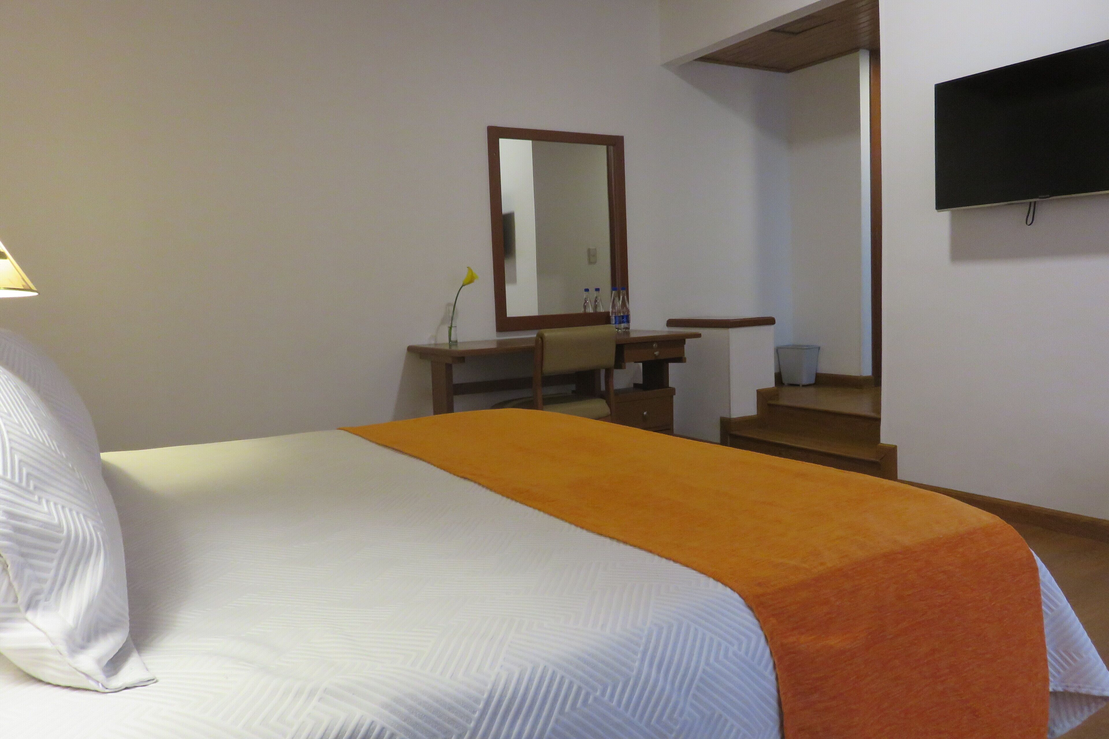 A hotel room with a bed, a desk, a mirror, a TV, and a staircase.