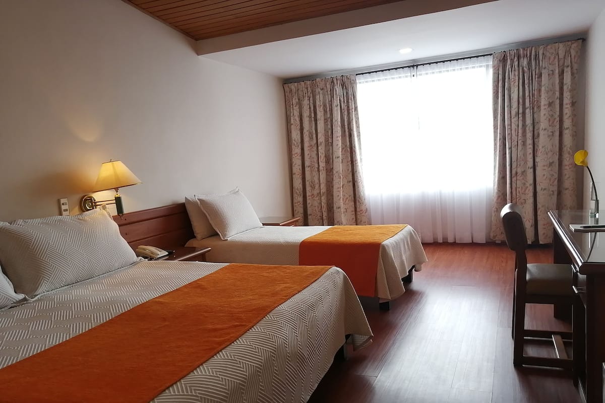 A hotel room with two beds, a desk, and a chair.