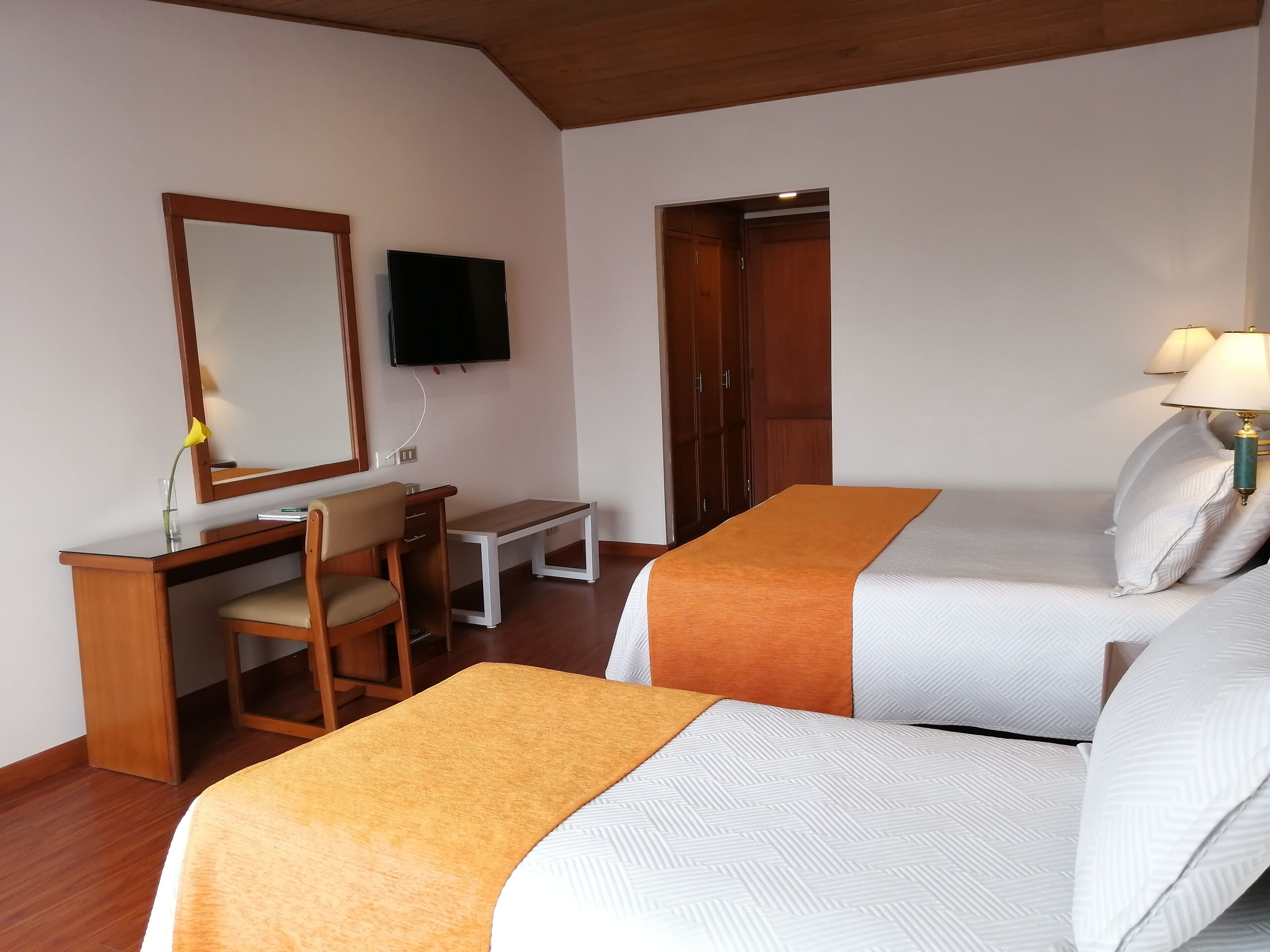 Habitación de hotel con dos camas, un escritorio, una silla, un televisor y un armario.