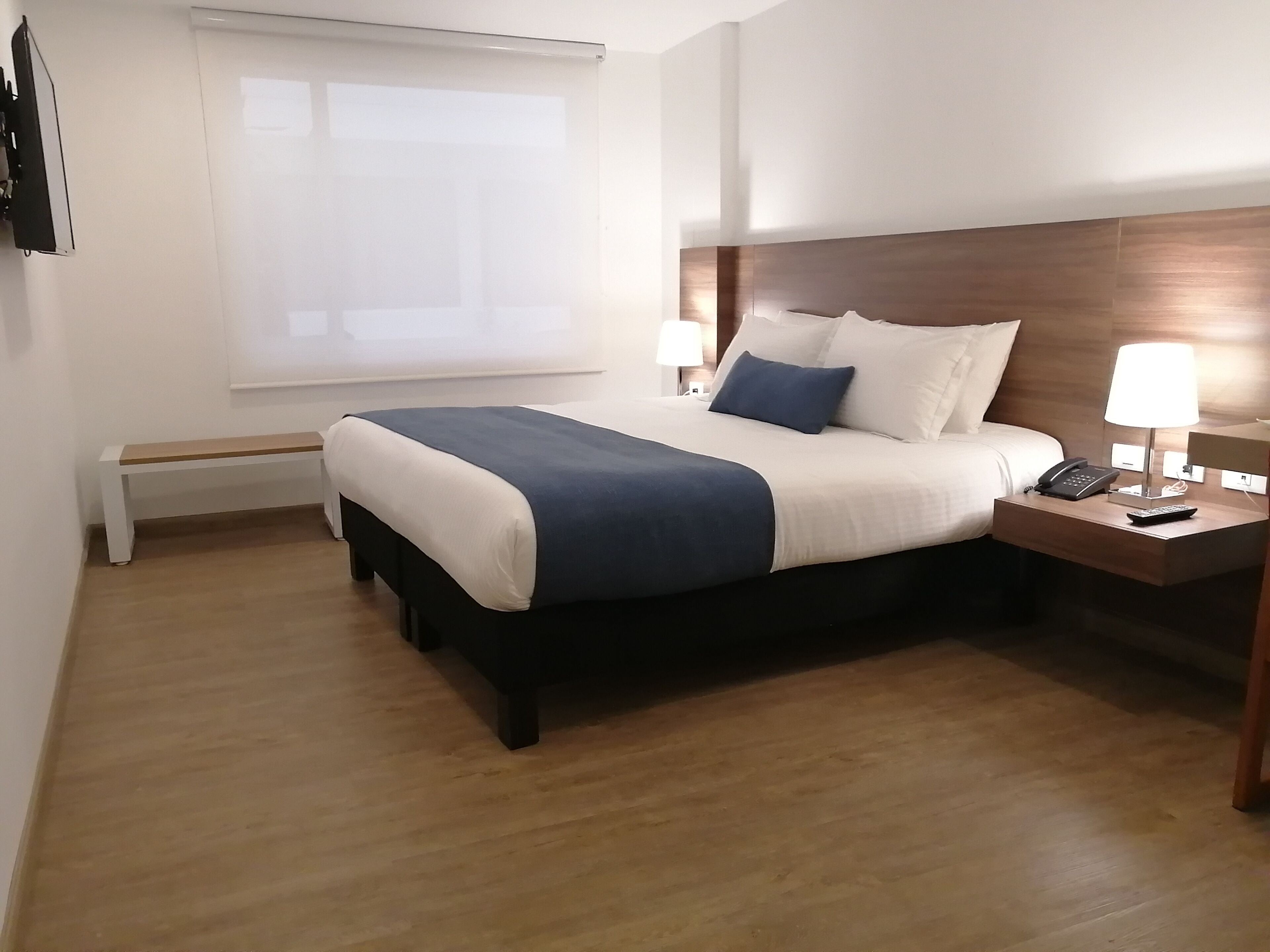 Quarto de hotel com cama, mesas de cabeceira, abajur e janela.