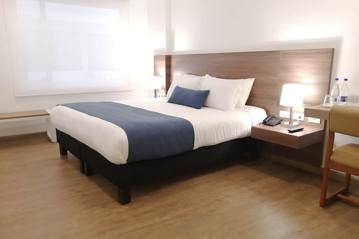 A neatly made bed with a blue and white bedspread, a wooden headboard, a bedside table with a lamp, and a chair.