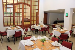 A dining area with multiple tables set for meals, red chairs, and a large wooden door with glass panels. - Hotel Daza (Paipa)
