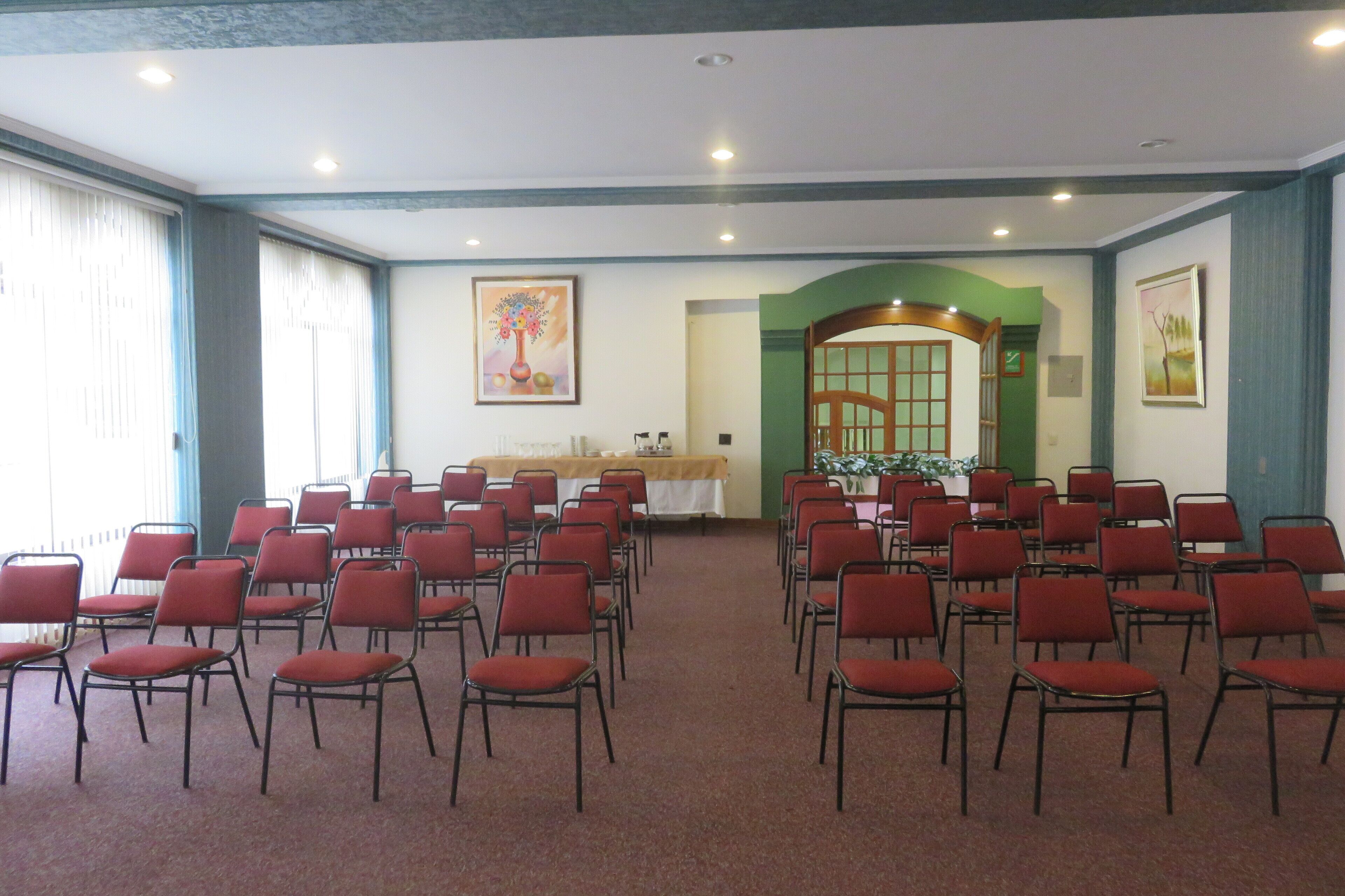 A conference room with rows of red chairs, a table with a white tablecloth, and two paintings on the walls.