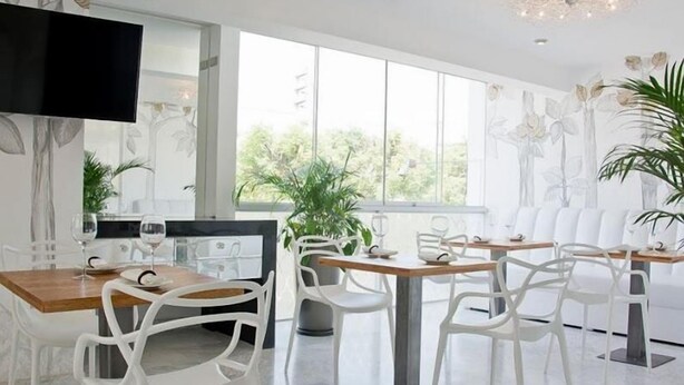 Un comedor moderno con sillas blancas y una mesa de madera, ventanas amplias y un televisor de pantalla plana.