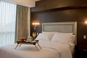 A hotel room with a large bed, a bedside table with a tray of breakfast items, a window with curtains, and wall-mounted lighting. - Arvo Hotel Boutique (Trujillo)