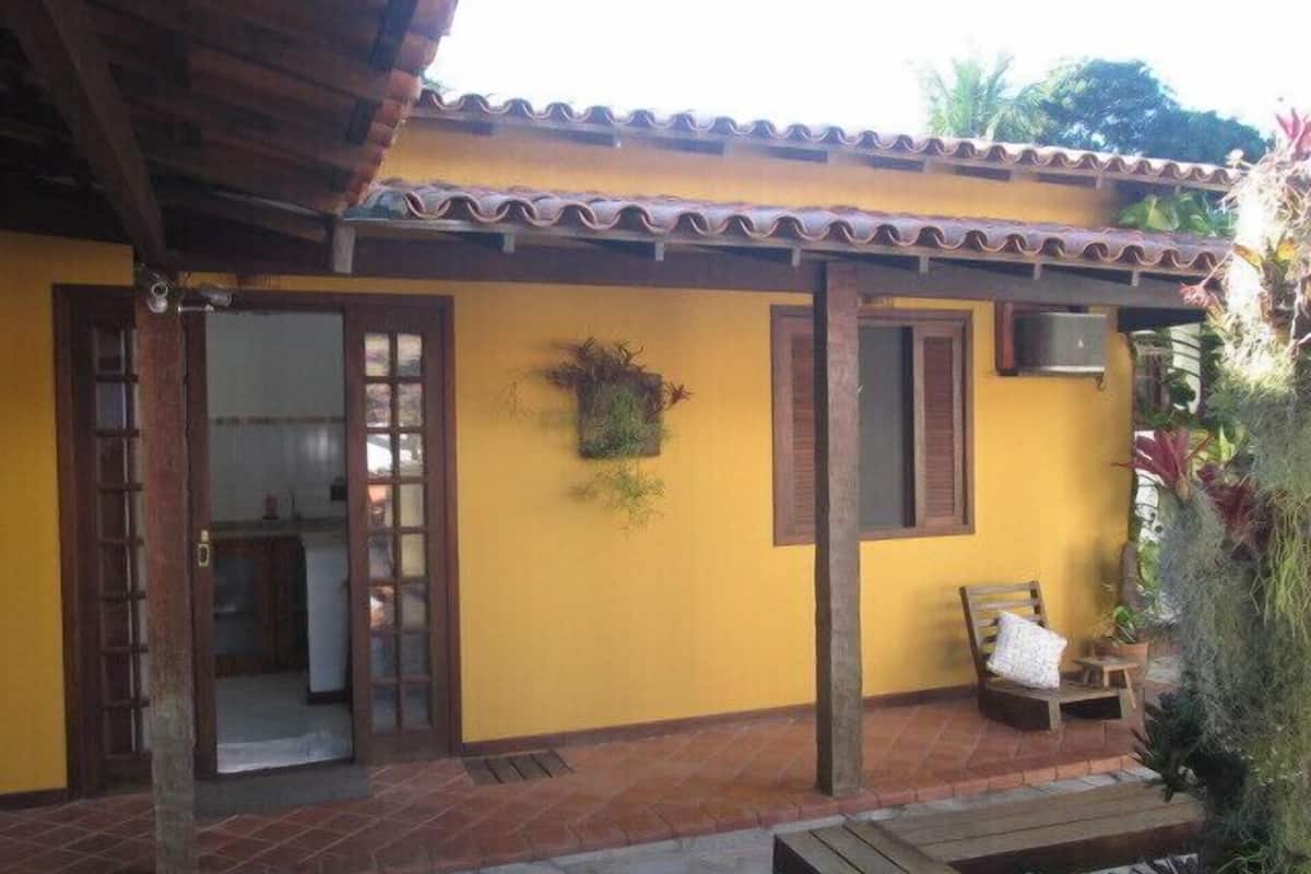 Un edificio amarillo con techo de tejas, puerta de madera y ventana con contraventanas.