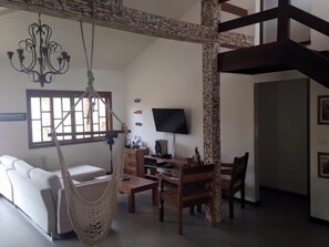 A spacious living area with a hammock, a white sofa, wooden furniture, a TV, and a stone-patterned column. - Maresia de Búzios Guest House (Buzios)