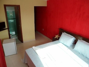 A hotel room with a bed, a small desk, and a red wall. - Pousada Enseada das Ancoras (Búzios)