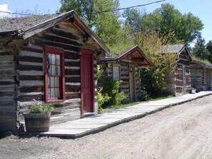 A row of log cabins with red doors and windows, a gravel driveway, and a wooden walkway. - Nevada City Hotel (Virginia City)