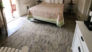 Quarto com cabeceira de madeira, cama com colcha estampada, mesa de cabeceira com abajur e cômoda.